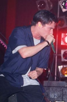 a young man singing into a microphone while sitting on a stool in front of a stage