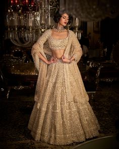 a woman in a gold lehenga standing next to a chandelier