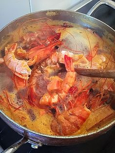 a pan filled with shrimp and other food on top of a stove next to a wooden spoon