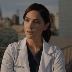 a woman in a white lab coat is looking off into the distance with buildings in the background