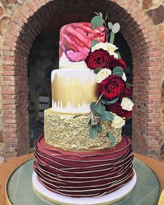 a multi layer cake with red and white flowers on the top is sitting in front of a brick oven