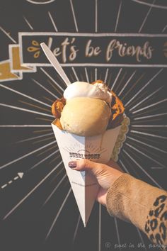 a person holding an ice cream cone in front of a sign that says let's be friends