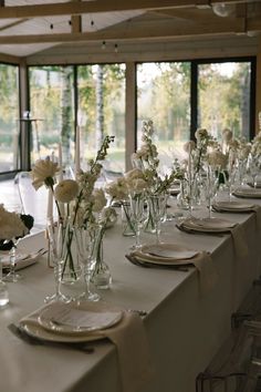 a long table is set with white flowers and place settings for an elegant dinner party