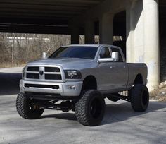 a silver truck is parked in front of a parking garage with large tires on it