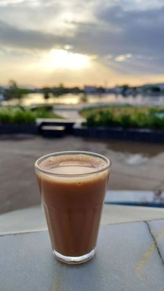 a cup of coffee sitting on top of a table next to a parking lot at sunset