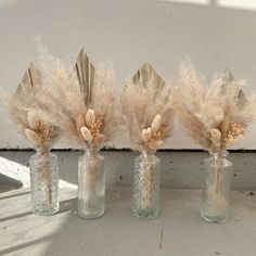 three glass vases with feathers in them on a ledge next to a window sill