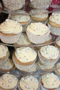 cupcakes with white frosting and pearls are on display in a glass case