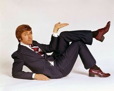 a man in a suit and tie laying on the ground with his legs crossed, wearing red shoes