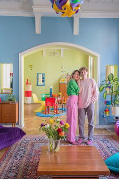 two people are standing in the living room with blue walls and colorful furnishings on the floor