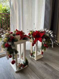 two christmas wreaths sitting on top of white wooden stands in front of a window