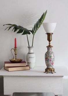 two vases and a candle are sitting on a white table with a plant in it