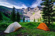 two tents set up on the side of a mountain overlooking a lake and mountains in the distance