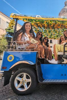 four women are sitting in the back of a blue golf cart