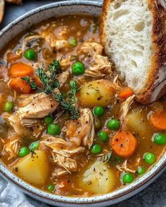 a bowl filled with chicken, carrots and peas next to a piece of bread