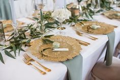 the table is set with gold plates, silverware and greenery for an elegant wedding reception