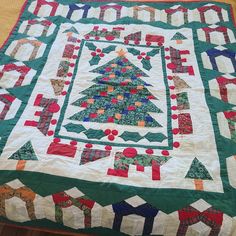 a quilted christmas tree is displayed on a table topper with ribbons and bows