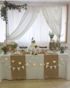 a table topped with lots of food and desserts next to a window covered in white drapes