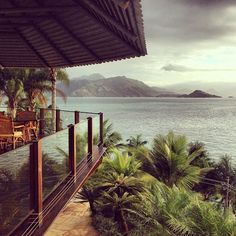 an ocean view with palm trees and chairs on the deck overlooking the water's edge