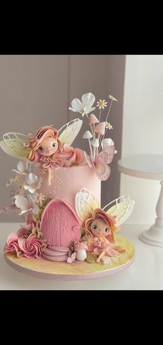 a pink cake decorated with flowers and fairy figurines