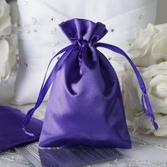 a purple satin bag sitting on top of a table next to white flowers and pillows