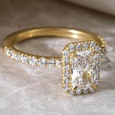 an engagement ring with a square cut diamond surrounded by smaller round diamonds on a marble surface