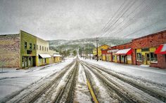 an empty street with snow on the ground and buildings in the backgrouds