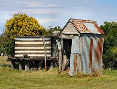 an old outhouse sits in the middle of a grassy field next to a shed