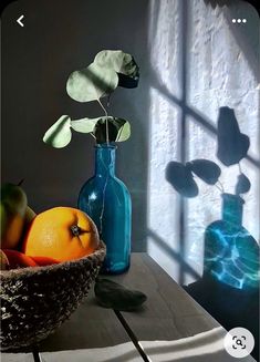 a table topped with blue vases filled with oranges and green apples next to a window