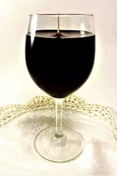 a glass of wine sitting on top of a white tablecloth with a black liquid in it