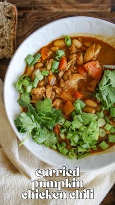 a white bowl filled with meat and vegetables on top of a wooden table next to bread