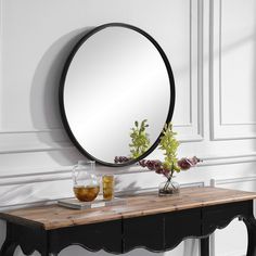 a round mirror sitting on top of a wooden table next to a vase with flowers