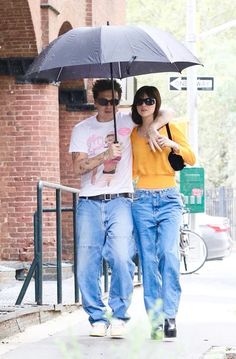 a man and woman walking down the street under an umbrella while holding each other's hand