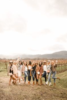 a group of young women standing next to each other in front of a vineyard fence