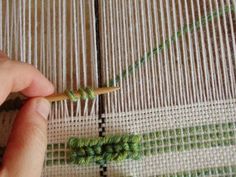 a hand is holding a piece of green thread on a bamboo mat that has been stitched together