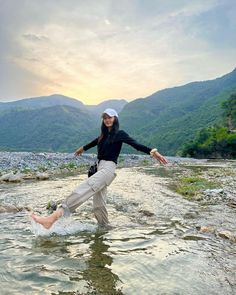 a woman standing in the middle of a river with her arms out and legs spread wide