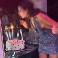 a woman blowing out candles on a cake with other people in the background at a party