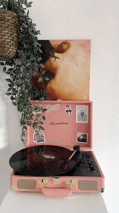 a record player sitting on top of a pink suitcase next to a potted plant