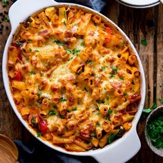 a white casserole dish filled with pasta and vegetables on top of a wooden table