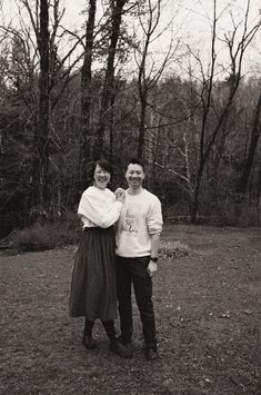 a man and woman standing next to each other in front of some trees with no leaves on them