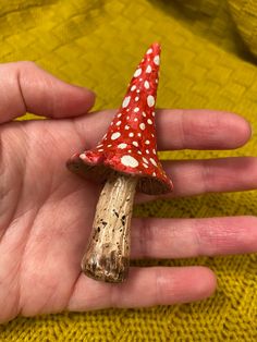 a small red and white mushroom sitting on top of someone's hand in front of a yellow sweater