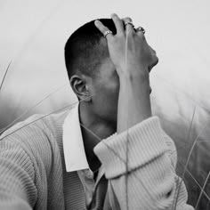 a black and white photo of a man holding his hand up to his face while standing in tall grass