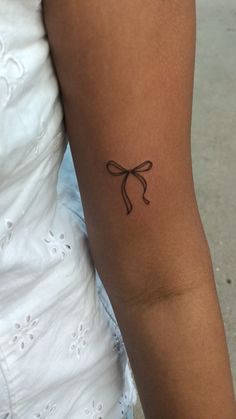 a woman's arm with a bow tattoo on the left side of her arm