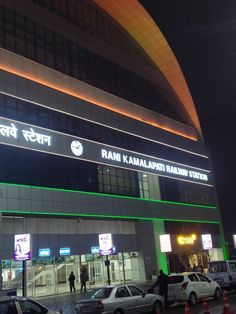 cars are parked in front of a building with neon lights on the side of it