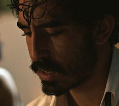 a close up of a person with a beard and wearing a white shirt looking at his cell phone