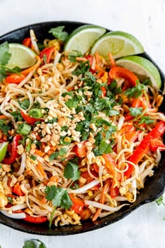 a bowl filled with noodles and vegetables on top of a white tablecloth next to lime wedges