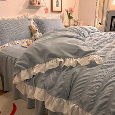 a teddy bear sitting on top of a bed with blue sheets and ruffled bedspread