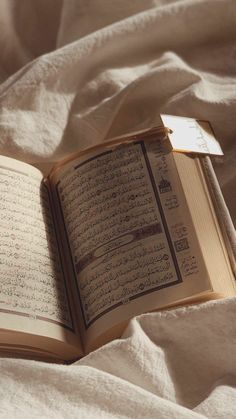 an open book laying on top of a white bed covered in sheets and blankets with arabic writing