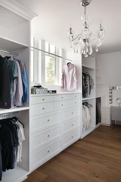 a white closet with clothes and chandelier hanging from the ceiling