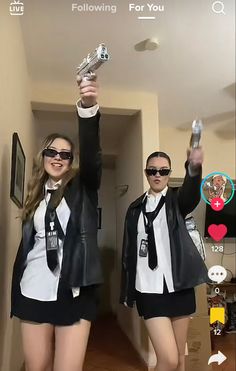 two girls in black and white outfits are holding up their cell phones while standing next to each other