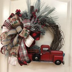 a wreath with a red truck and pine cones on it is hung on the front door